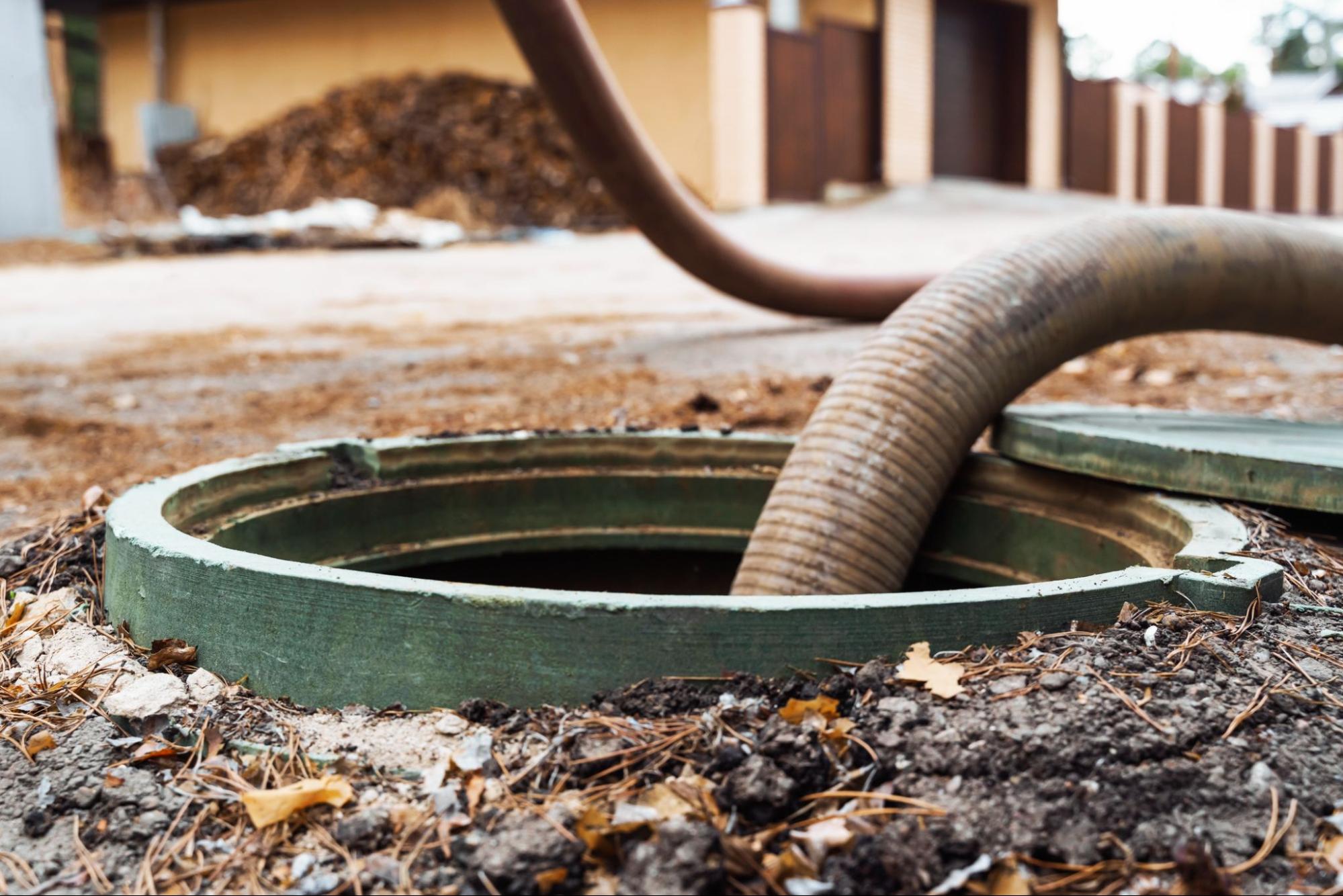 Vacuum hose pumping an open septic tank during alternative septic system maintenance
